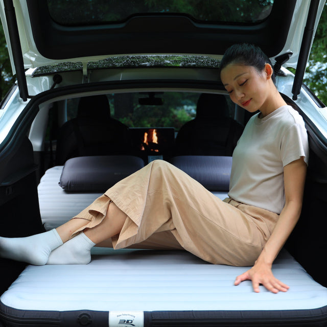 女子舒適地坐在鋪有 3D Mats 卡好眠充氣床墊的行李廂內,車尾門開著
